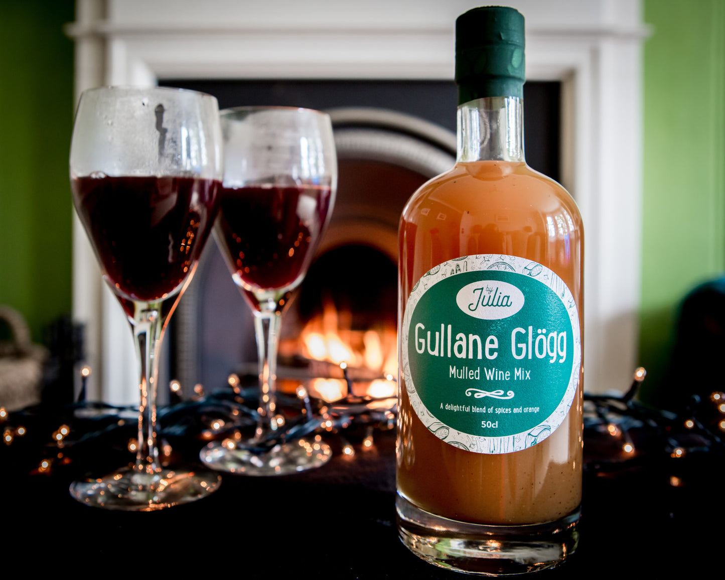 Gullane Glögg Mulled Wine Mix and two glasses of mulled wine in front of fire