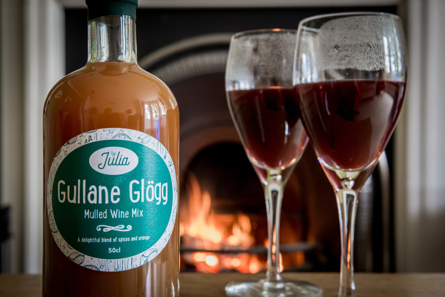 Gullane Glögg Mulled Wine Mix and two glasses of mulled wine in front of fire